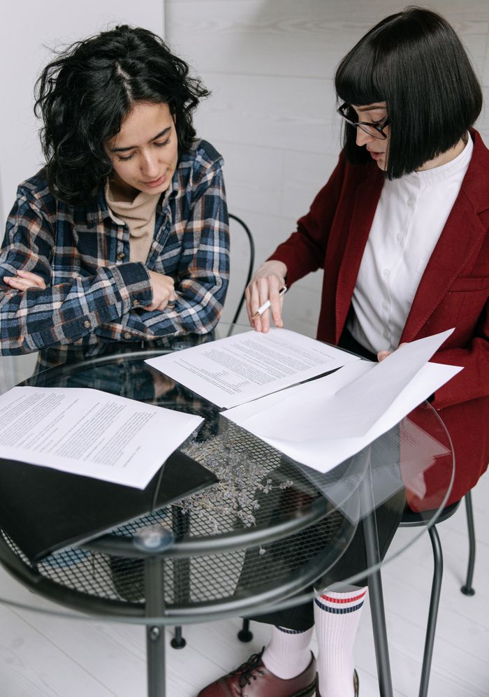 about-us-01 Two professional women discussing and reviewing documents during a meeting indoors.